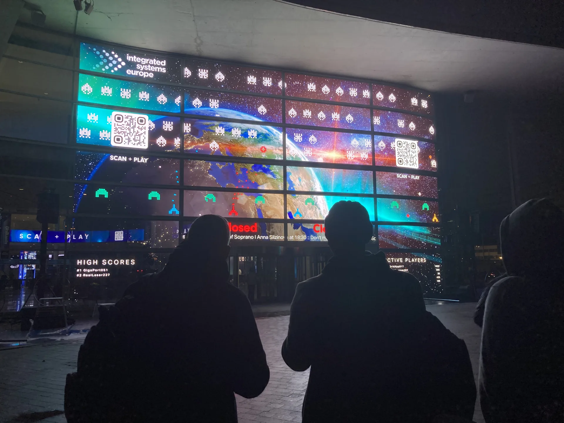 Besucher vor der LED-Wand mit Spielfeld, QR-Codes und Highscore